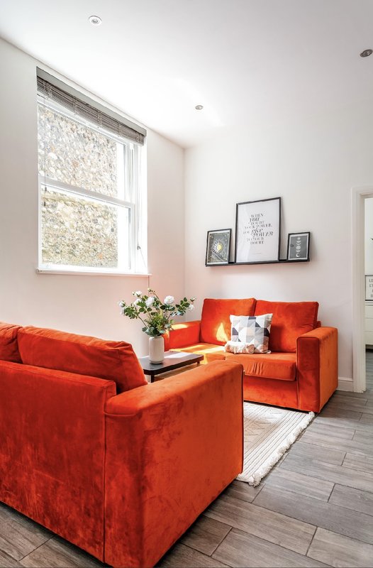 Bright living room with two red upholstered sofas, white flowers, framed wall art and large window