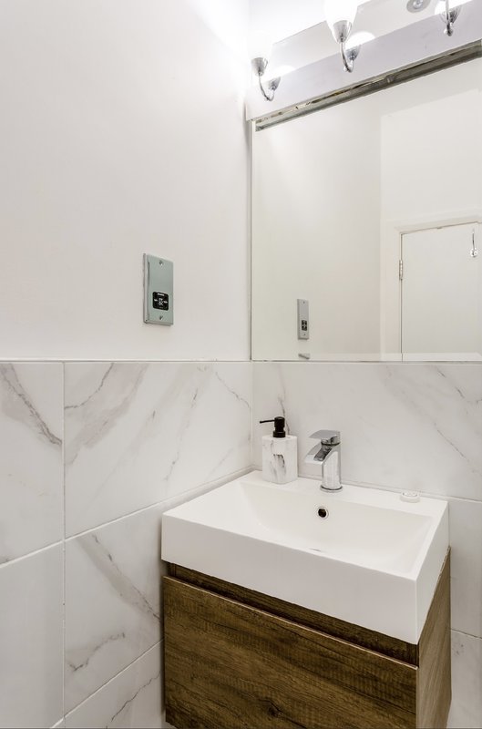 Modern bathroom with marble tile walls, white sink, wooden vanity, and mirror.