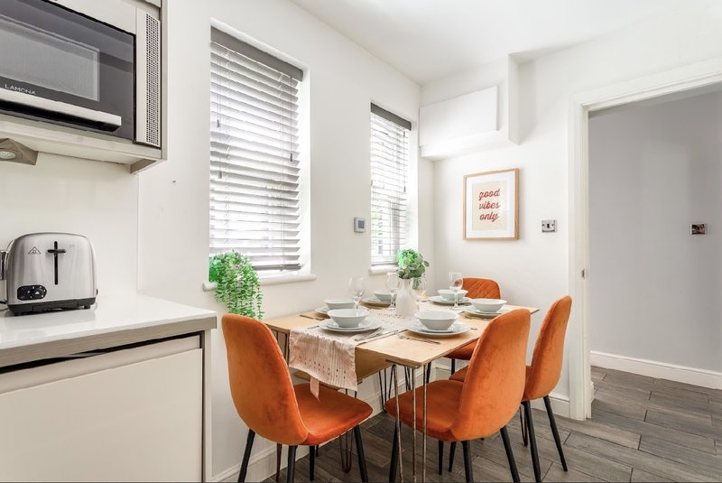 Bright kitchen-diner with white cabinetry, dining table, orange chairs and potted plants