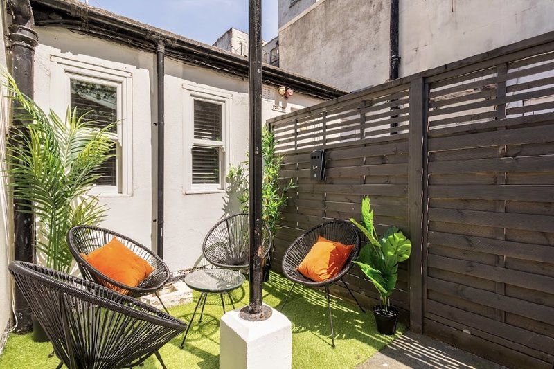 Small outdoor patio with woven chairs, potted plants, and wooden privacy fence