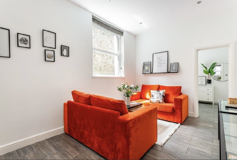 Bright living room with orange velvet seating, framed wall art, potted plant and window light