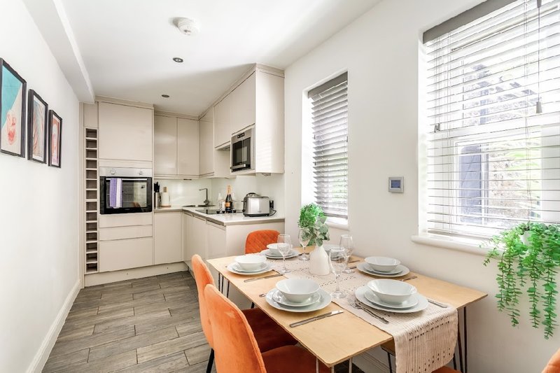 Modern kitchen-diner with cream cabinetry, wooden table, orange chairs and green plant