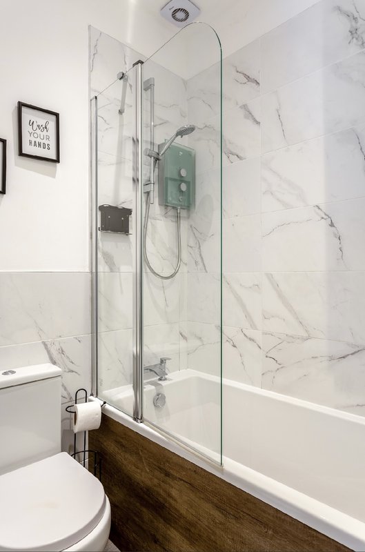 Modern bathroom with marble-tiled shower enclosure, white toilet, and wooden vanity base