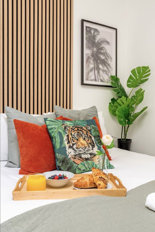 Bedroom with decorative pillows, potted plant, framed wall art, and breakfast tray on bed