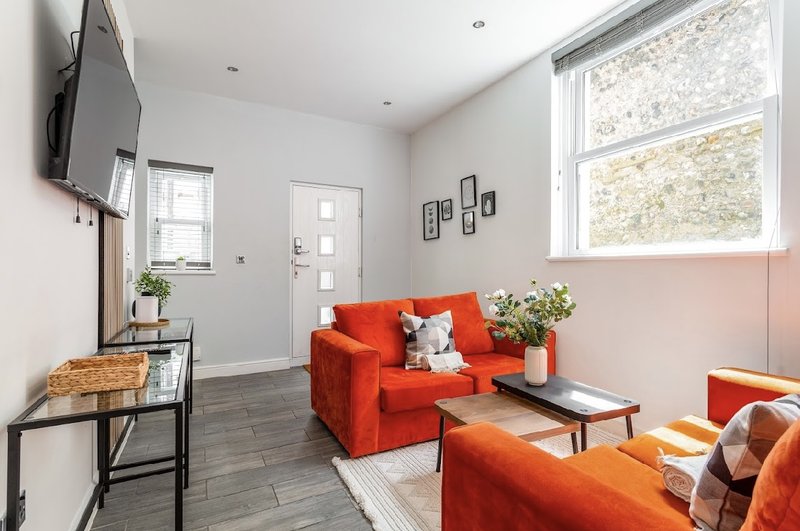 Living room with red sofas, TV on wall, large windows, wooden floor and potted plants