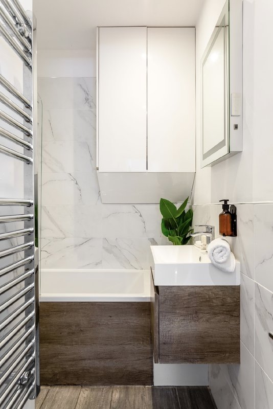 Modern bathroom with marble-tiled walls, dark wood vanity, white sink and mirrored cabinet above