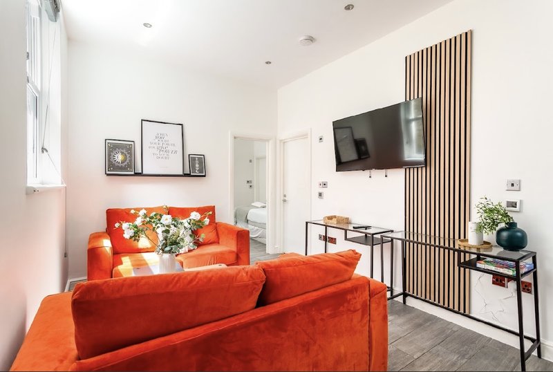 Modern living room with bright orange sofa, wall-mounted TV, wooden slat feature wall and framed artwork