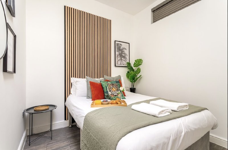 Compact bedroom with single bed, colorful cushions, potted plant, and wooden wall paneling