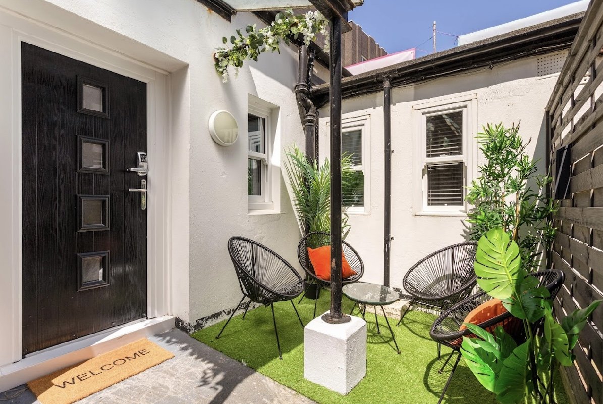 Outdoor patio entrance with black door, two wire chairs, potted plants and artificial turf
