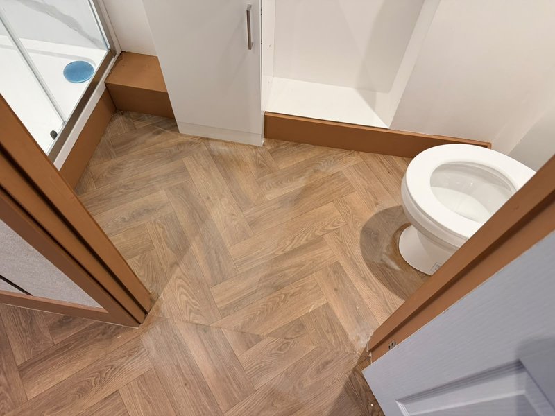 Bathroom with herringbone wood-effect flooring, white toilet, and wooden door frames