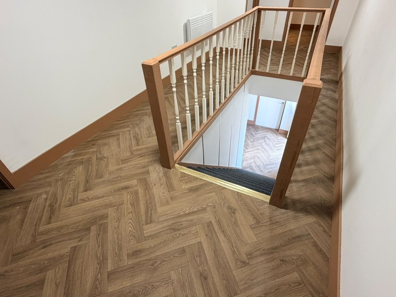 Staircase landing with wooden herringbone flooring, wooden railings, and skylight opening