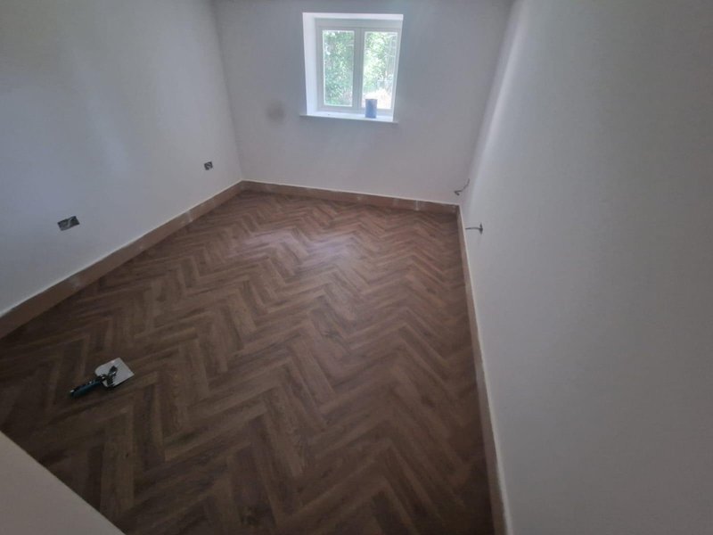 Empty room with herringbone wood flooring, white walls, and high window