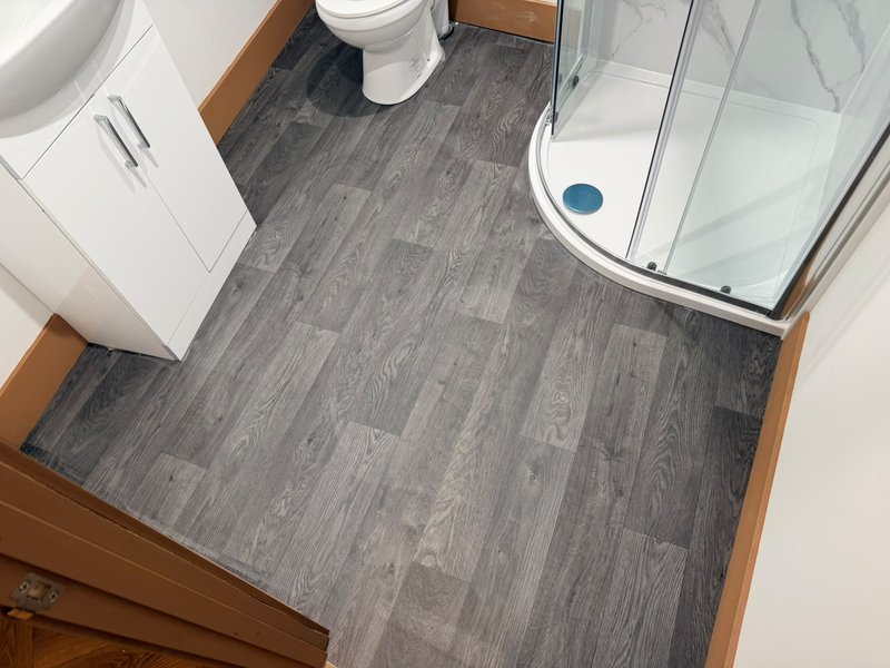 Modern bathroom with toilet, vanity, shower enclosure and grey wood-effect flooring