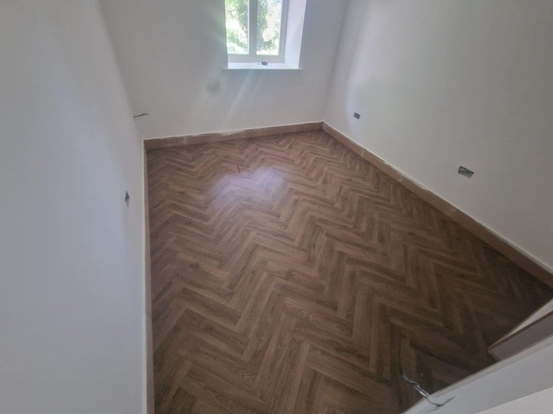 Empty room with herringbone wooden flooring, white walls and small window