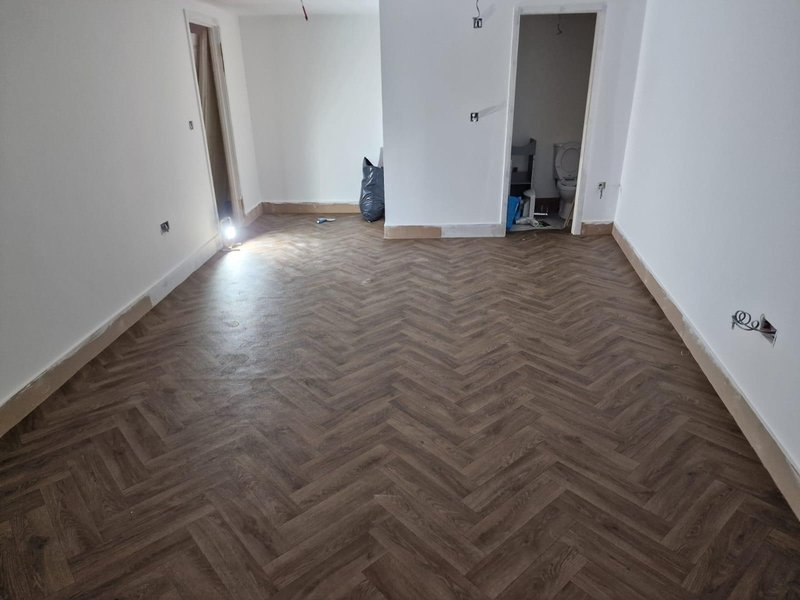 Empty room with herringbone wood flooring, white walls, and open doorways