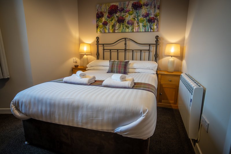 Bedroom with double bed, metal headboard, bedside lamps, wooden nightstand and floral wall art