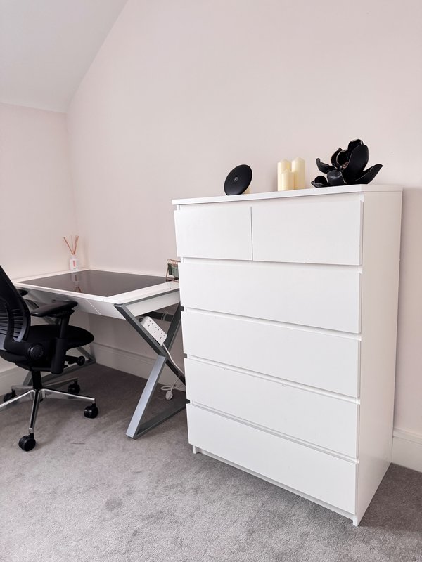 Modern home office with white desk, black office chair, and white multi-drawer dresser