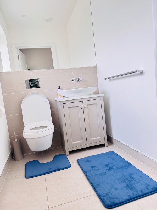 Modern bathroom with white toilet, vanity cabinet, sink, and blue bath mats on tile floor