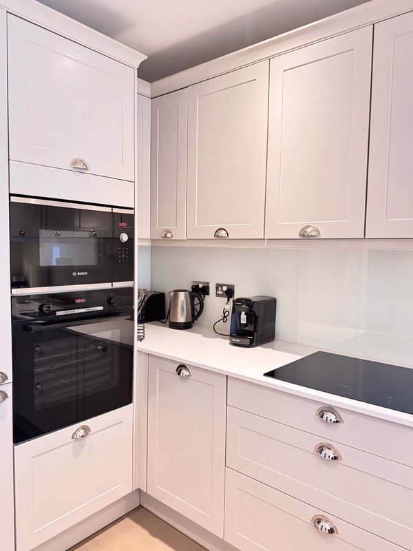 Modern pink kitchen with white cabinetry, black built-in oven, and countertop appliances