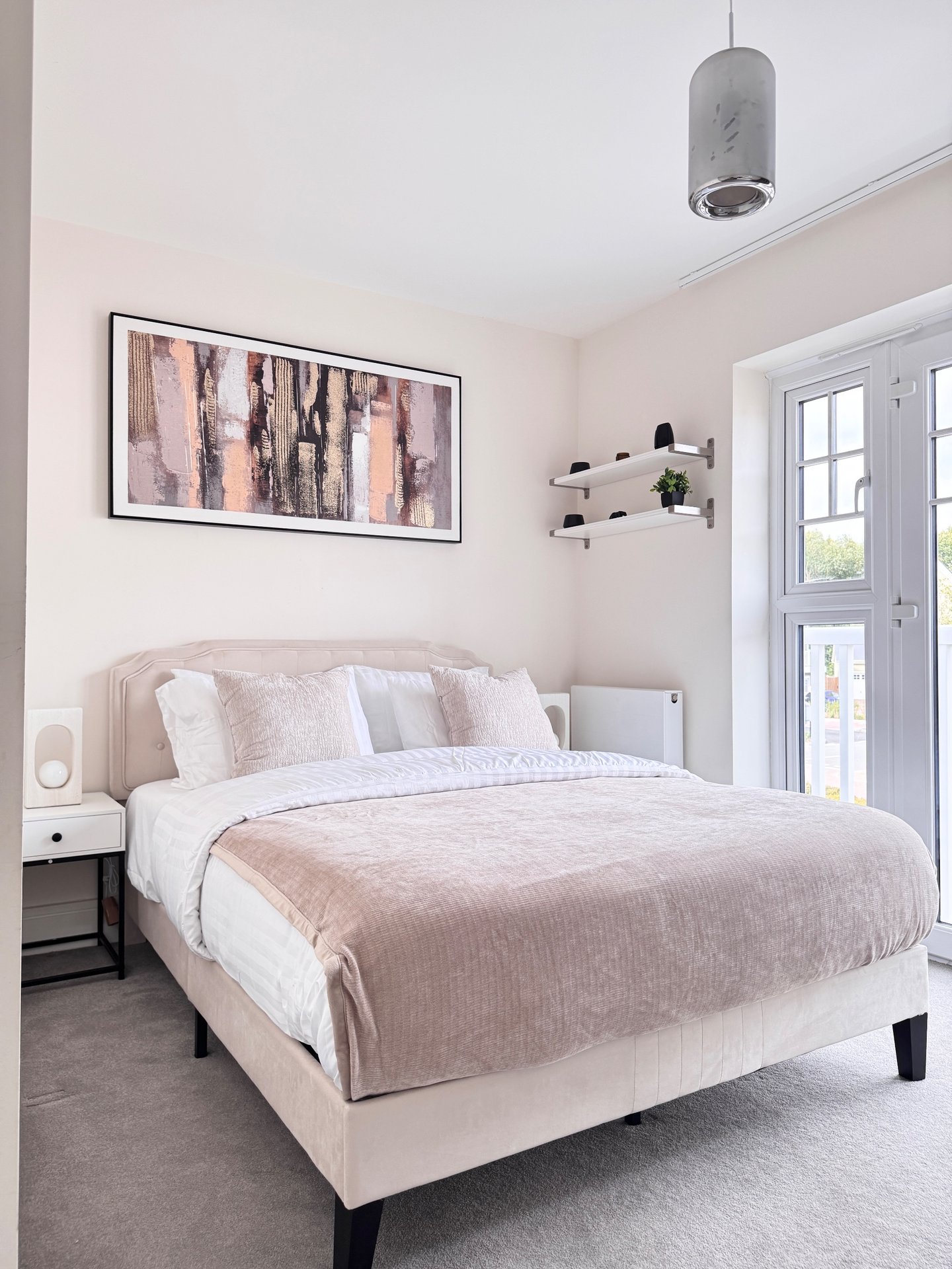 Modern bedroom with cream upholstered bed, white bedding, abstract wall art and pendant light