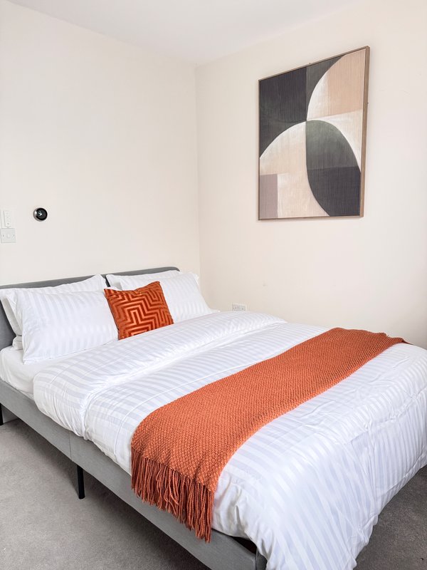 Modern bedroom with double bed, white striped bedding, orange throw, and geometric wall art