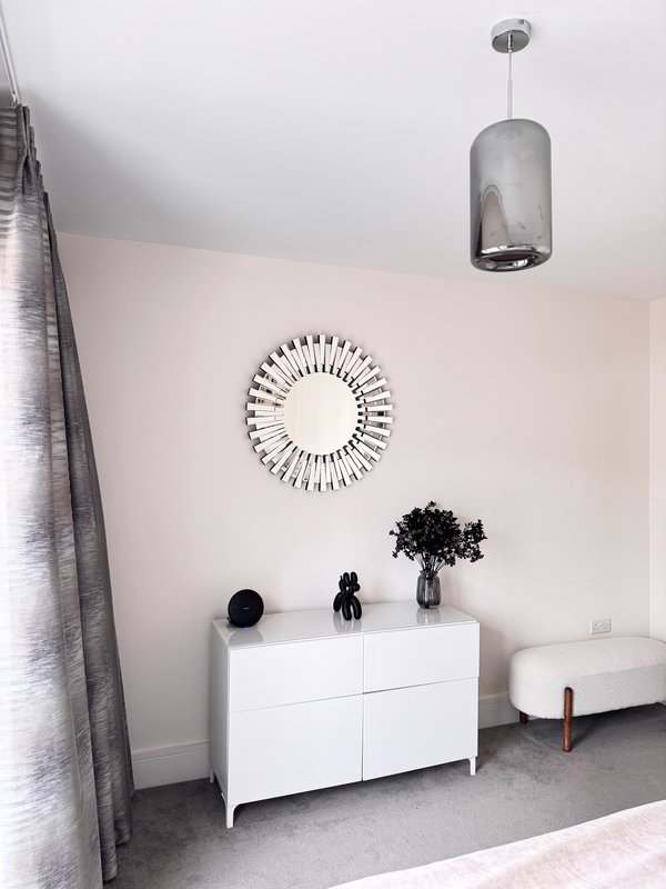Minimalist bedroom with white dresser, circular mirror, pendant light and grey carpet