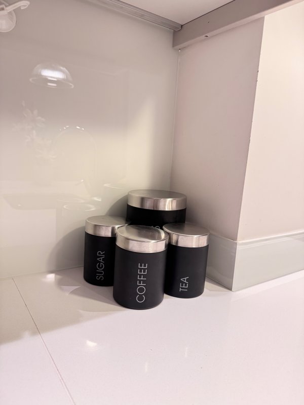 Kitchen counter with four black storage canisters labeled sugar, coffee, and tea