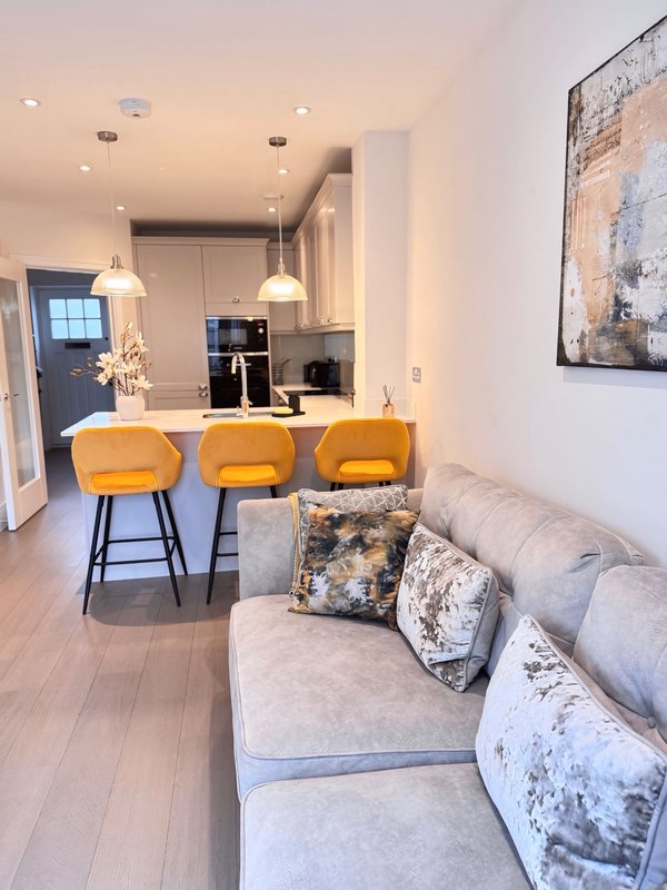 Open-plan living area with gray sofa, three yellow bar stools, kitchen counter, and modern pendant lighting
