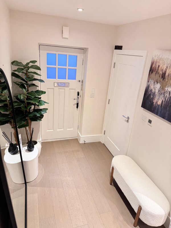 Bright entryway with white doors, potted plant, bench seating, and framed wall art