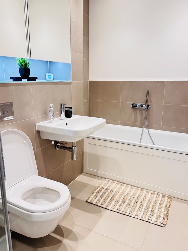 Modern bathroom with toilet, wall-mounted sink, bathtub and blue tile accent wall