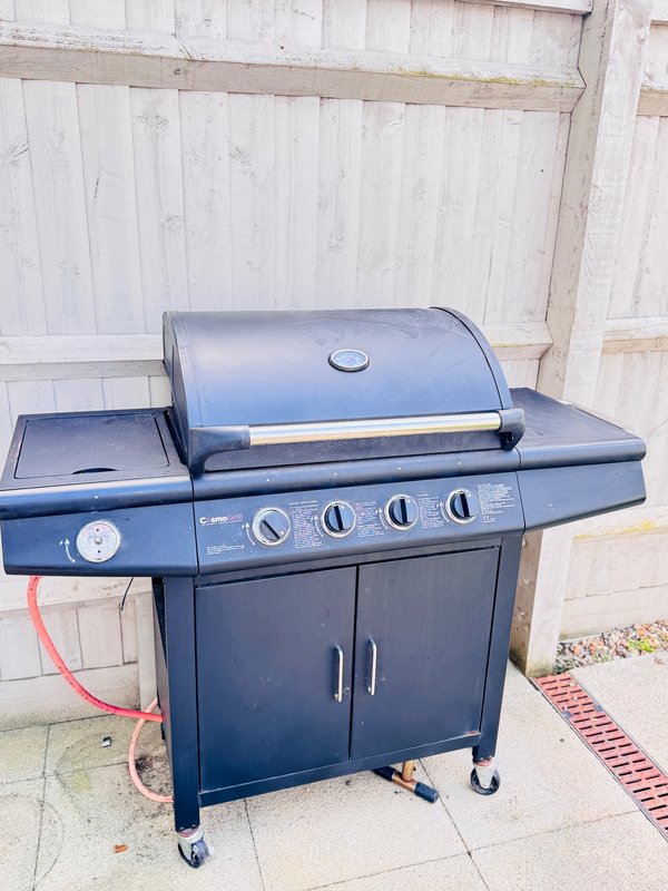 Black gas barbecue grill with lid on patio against white wooden fence