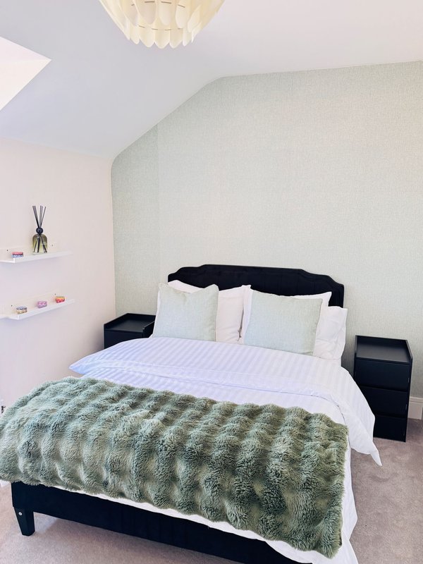 Modern bedroom with double bed, green throw blanket, white pillows and cream ceiling light