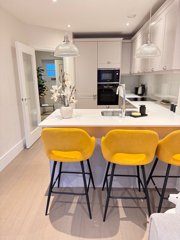 Modern kitchen with white cabinetry, island, yellow bar stools, pendant lights and built-in appliances