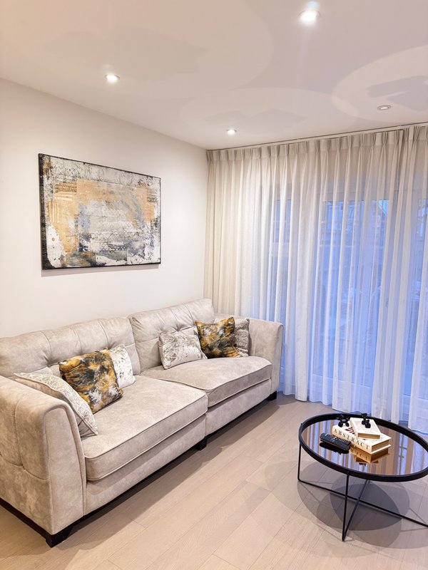 Modern living room with beige sofa, decorative pillows, wall art, and vertical blinds