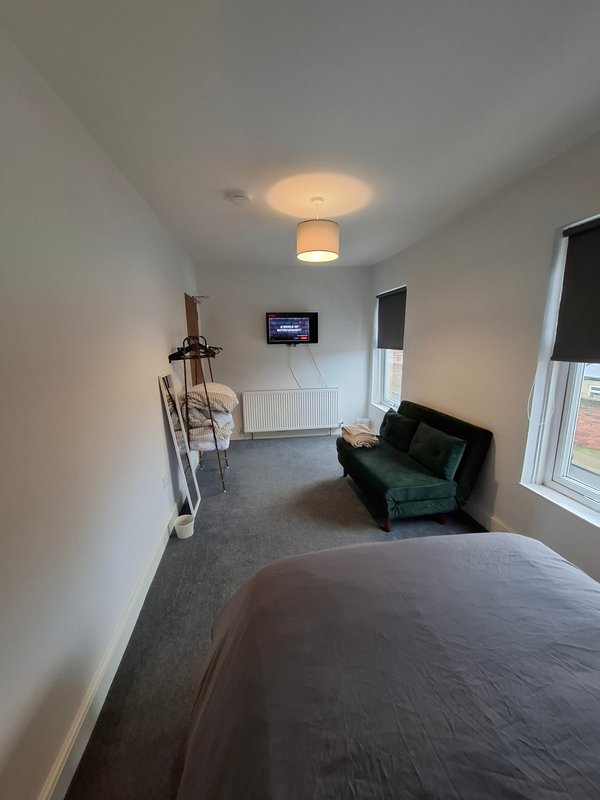 Studio bedroom with double bed, green sofa, wall-mounted TV, ceiling light and window