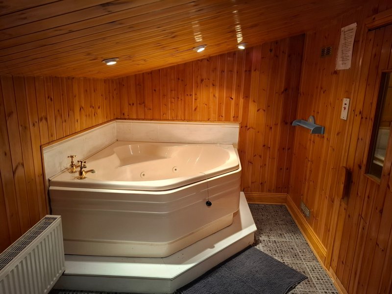 Wooden bathroom with corner spa bath, heated towel rail and recessed lighting