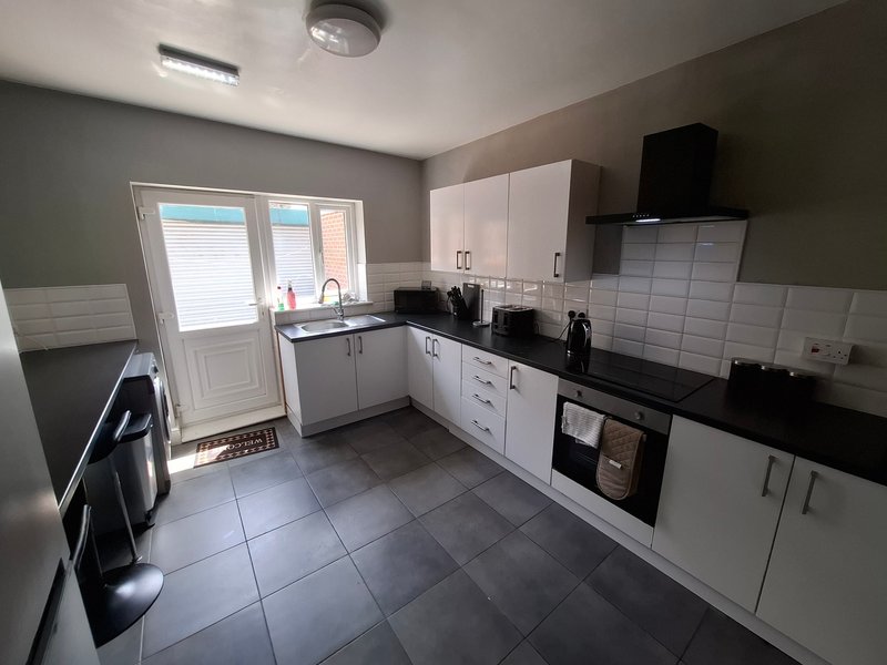 Modern kitchen with white cabinets, black countertops, tiled flooring and patio doors