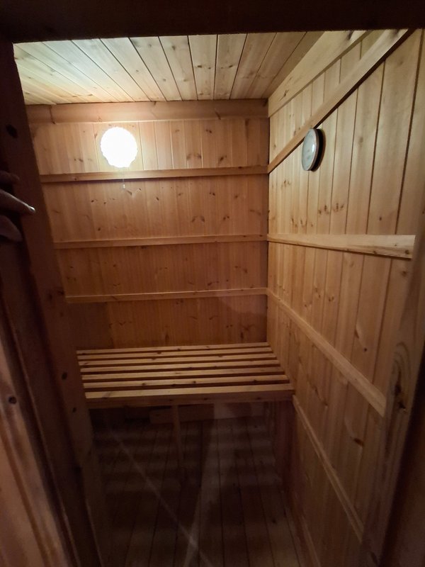 Interior of wooden sauna with bench seating, round window and ladle on wall