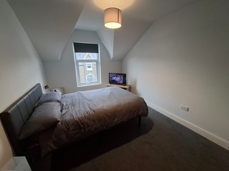 Attic bedroom with double bed, window, ceiling light, and small TV on shelf