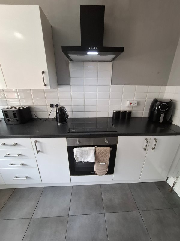 Modern kitchen with white cabinetry, black countertop, range hood and tiled backsplash