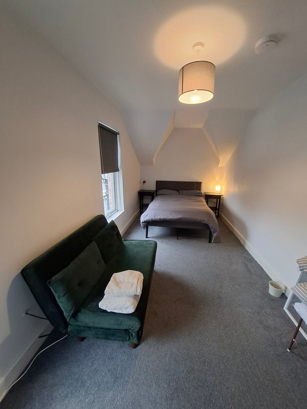 Narrow bedroom with single bed, green armchair, ceiling lamp, and small window
