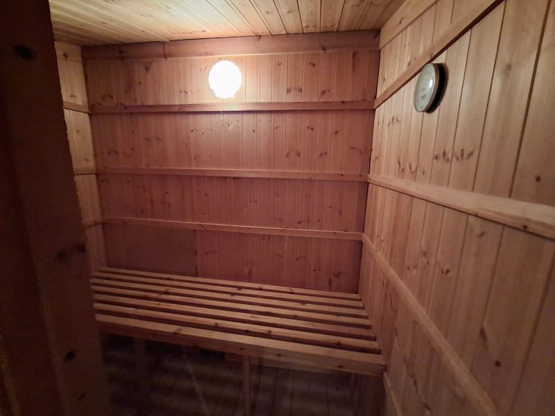 Interior of wooden sauna with benches, light fixture and clock on wall