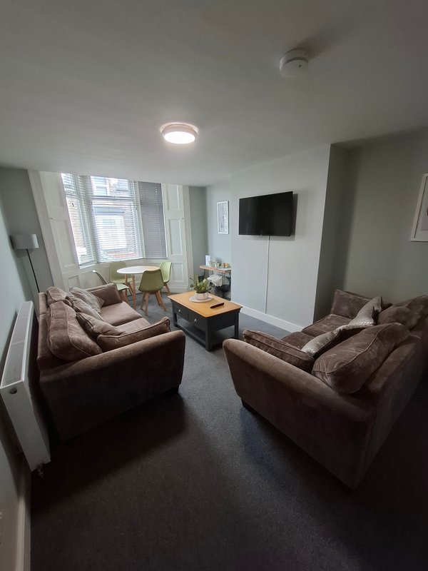 Modern living room with brown sofas, wall-mounted TV, coffee table and large windows