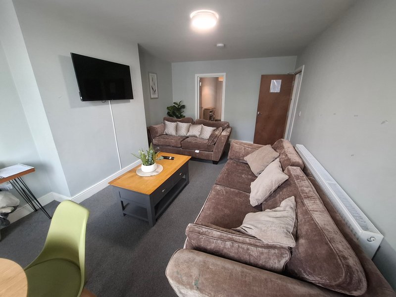 Living room with two brown sofas, wooden coffee table, wall-mounted TV, and modern lighting