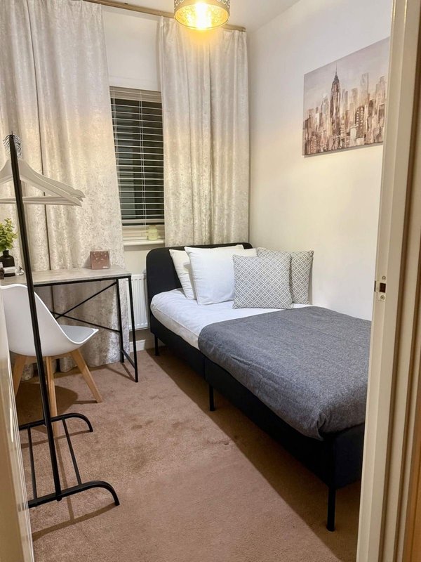 Compact bedroom with single bed, desk chair, pendant light and city skyline artwork