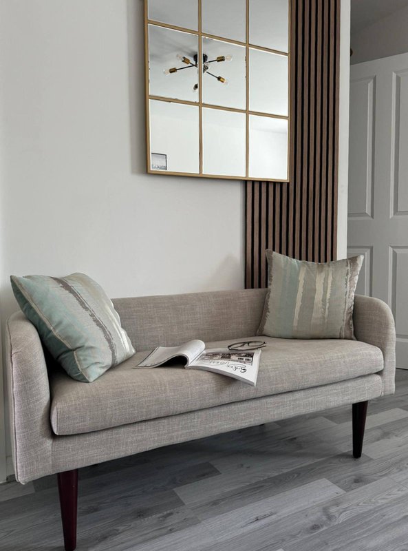Modern living room with grey upholstered sofa, decorative pillows, mirror, and curtains