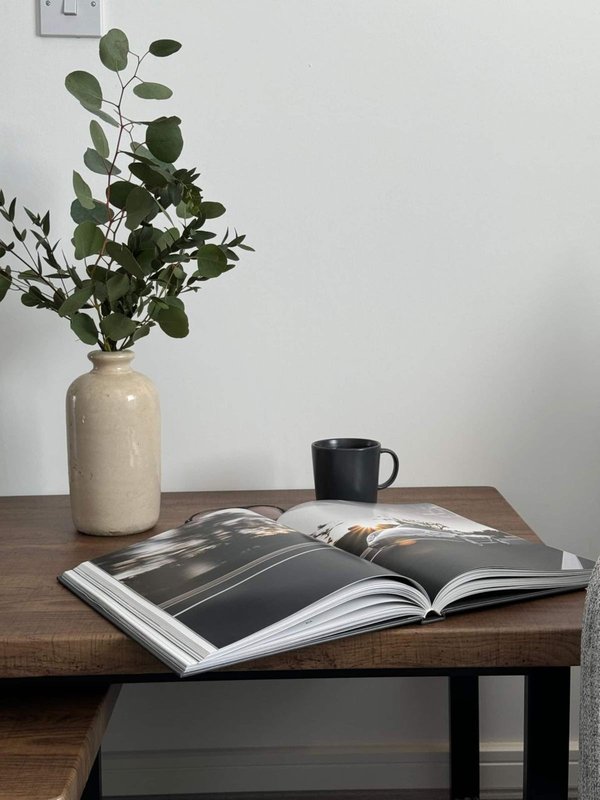 Wooden table with open magazine, ceramic vase with green foliage, and black mug