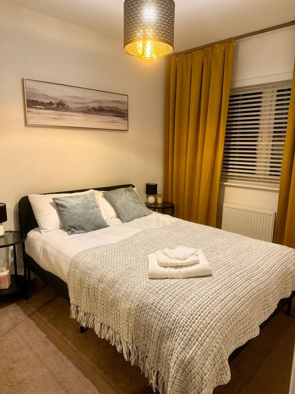 Bedroom with double bed, white bedding, gold curtains, framed artwork and ceiling lamp