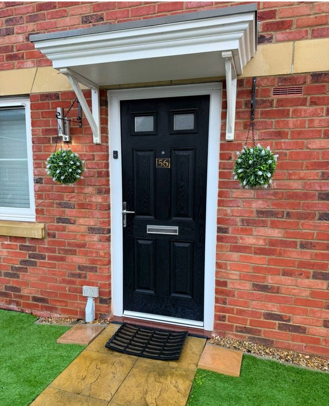 Red brick house exterior with black front door, white portico, and potted plants flanking entrance