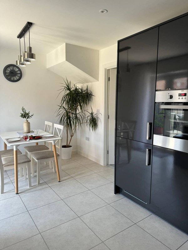 Modern kitchen with black cabinetry, dining table, potted plant, and wall clock
